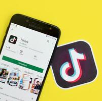 Tiktok application in playmarket on samsung smartphone screen on yellow background. TikTok is a popular video-sharing social networking service owned by ByteDance photo