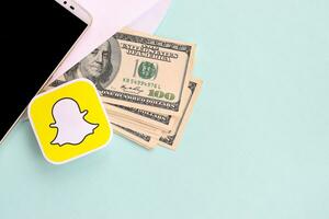 Snapchat paper logo lies with envelope full of dollar bills and smartphone photo