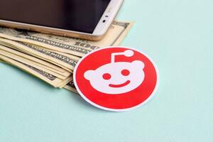 Reddit paper logo lies with envelope full of dollar bills and smartphone photo