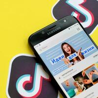 Tiktok application on samsung smartphone screen on yellow background. TikTok is a popular video-sharing social networking service owned by ByteDance photo