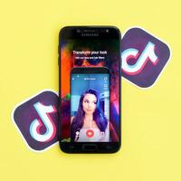 Tiktok application on samsung smartphone screen on yellow background. TikTok is a popular video-sharing social networking service owned by ByteDance photo