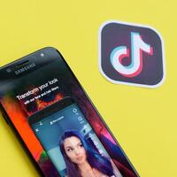 Tiktok application on samsung smartphone screen on yellow background. TikTok is a popular video-sharing social networking service owned by ByteDance photo