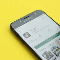 Tiktok application in playmarket on samsung smartphone screen on yellow background. TikTok is a popular video-sharing social networking service owned by ByteDance photo