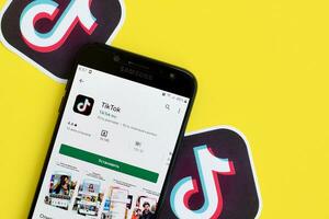 Tiktok application in playmarket on samsung smartphone screen on yellow background. TikTok is a popular video-sharing social networking service owned by ByteDance photo