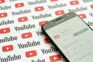 Youtube app on samsung smartphone screen on paper banner with small youtube logos and inscriptions. YouTube is Google subsidiary and American most popular video-sharing platform photo