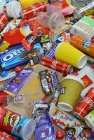 Big pile of many disposable colored trash from edible products of famous food and beverage manufacturers. Soda cans and chocolate bar wrappings in stack photo