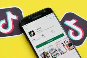 Tiktok application in playmarket on samsung smartphone screen on yellow background. TikTok is a popular video-sharing social networking service owned by ByteDance photo