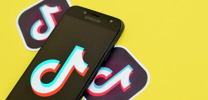 Tiktok logo on samsung smartphone screen on yellow background. TikTok is a popular video-sharing social networking service owned by ByteDance photo
