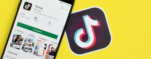 Tiktok application in playmarket on samsung smartphone screen on yellow background. TikTok is a popular video-sharing social networking service owned by ByteDance photo