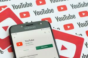 Youtube app on samsung smartphone screen on paper banner with small youtube logos and inscriptions. YouTube is Google subsidiary and American most popular video-sharing platform photo