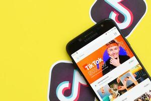 Tiktok application on samsung smartphone screen on yellow background. TikTok is a popular video-sharing social networking service owned by ByteDance photo