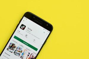 Tiktok application in playmarket on samsung smartphone screen on yellow background. TikTok is a popular video-sharing social networking service owned by ByteDance photo