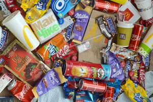 Big pile of many disposable colored trash from edible products of famous food and beverage manufacturers. Soda cans and chocolate bar wrappings in stack photo