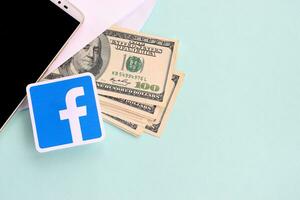 Facebook paper logo lies with envelope full of dollar bills and smartphone photo