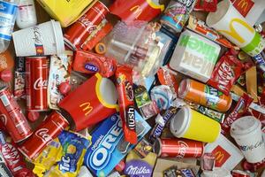 Big pile of many disposable colored trash from edible products of famous food and beverage manufacturers. Soda cans and chocolate bar wrappings in stack photo