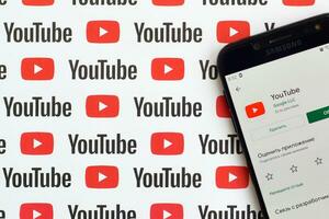 Youtube app on samsung smartphone screen on paper banner with small youtube logos and inscriptions. YouTube is Google subsidiary and American most popular video-sharing platform photo