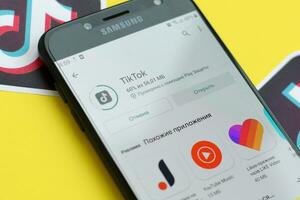 Tiktok application in playmarket on samsung smartphone screen on yellow background. TikTok is a popular video-sharing social networking service owned by ByteDance photo