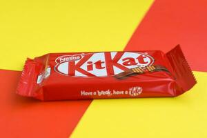 Kit Kat chocolate bars in red wrapping lies on yellow and red background. Kit kat created by Rowntree's of York in United Kingdom and is now produced globally by Nestle photo