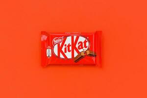 Kit Kat chocolate bar in red wrapping lies on red background. Kit kat created by Rowntree's of York in United Kingdom and is now produced globally by Nestle photo