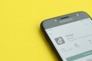 Tiktok application in playmarket on samsung smartphone screen on yellow background. TikTok is a popular video-sharing social networking service owned by ByteDance photo