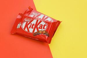 Kit Kat chocolate bars in red wrapping lies on yellow and red background. Kit kat created by Rowntree's of York in United Kingdom and is now produced globally by Nestle photo