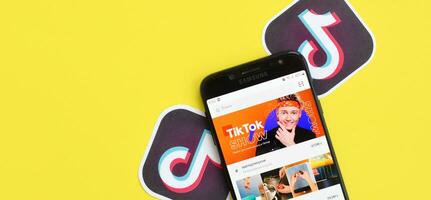 Tiktok application on samsung smartphone screen on yellow background. TikTok is a popular video-sharing social networking service owned by ByteDance photo