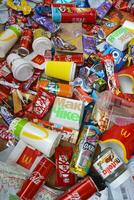 Big pile of many disposable colored trash from edible products of famous food and beverage manufacturers. Soda cans and chocolate bar wrappings in stack photo