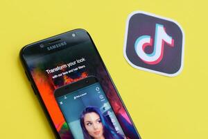 Tiktok application on samsung smartphone screen on yellow background. TikTok is a popular video-sharing social networking service owned by ByteDance photo