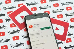 Youtube app on samsung smartphone screen on paper banner with small youtube logos and inscriptions. YouTube is Google subsidiary and American most popular video-sharing platform photo