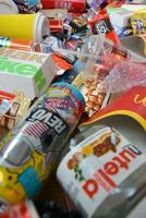 Big pile of many disposable colored trash from edible products of famous food and beverage manufacturers. Soda cans and chocolate bar wrappings in stack photo