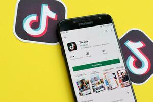 Tiktok application in playmarket on samsung smartphone screen on yellow background. TikTok is a popular video-sharing social networking service owned by ByteDance photo
