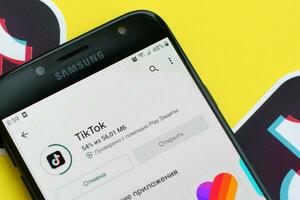 Tiktok application in playmarket on samsung smartphone screen on yellow background. TikTok is a popular video-sharing social networking service owned by ByteDance photo