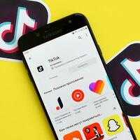 Tiktok application in playmarket on samsung smartphone screen on yellow background. TikTok is a popular video-sharing social networking service owned by ByteDance photo