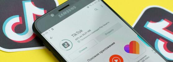 Tiktok application in playmarket on samsung smartphone screen on yellow background. TikTok is a popular video-sharing social networking service owned by ByteDance photo
