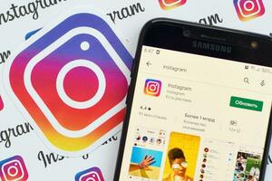 Instagram app on samsung smartphone screen on banner with small instagram logos. Instagram is American photo and video-sharing social networking service by Facebook inc
