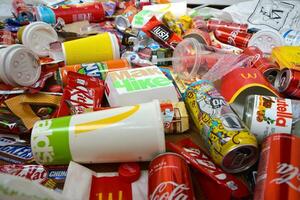 Big pile of many disposable colored trash from edible products of famous food and beverage manufacturers. Soda cans and chocolate bar wrappings in stack photo