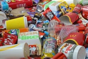 Big pile of many disposable colored trash from edible products of famous food and beverage manufacturers. Soda cans and chocolate bar wrappings in stack photo