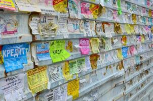 KHARKOV, UKRAINE - JUNE 24, 2018 Grunge Message Board with many advertisement. People spreading advertising and information on white paper than post it on metal fence photo