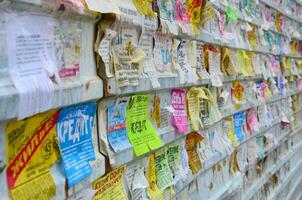 KHARKOV, UKRAINE - JUNE 24, 2018 Grunge Message Board with many advertisement. People spreading advertising and information on white paper than post it on metal fence photo