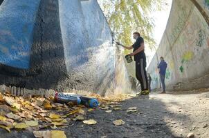 KHARKOV, UKRAINE - OCTOBER 19, 2019 Dope used spray cans for graffiti painting outdoors in autumn leafs and artist in painting process photo