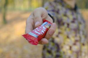 KHARKOV, UKRAINE - OCTOBER 21, 2019 Young man passes a Kit kat chocolate bar in an autumn park. The manifestation of kindness, treating with sweets photo