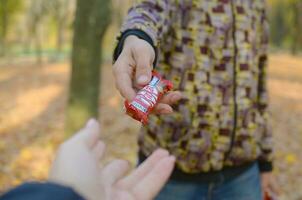 KHARKOV, UKRAINE - OCTOBER 21, 2019 Male hand passes the girl a Kit kat chocolate bar in an autumn park. The manifestation of kindness, treating with sweets photo