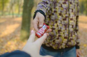 KHARKOV, UKRAINE - OCTOBER 21, 2019 Male hand passes the girl a Kit kat chocolate bar in an autumn park. The manifestation of kindness, treating with sweets photo