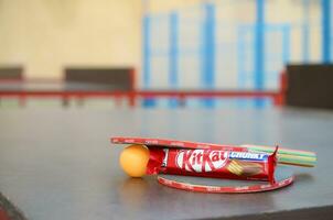 KHARKOV, UKRAINE - OCTOBER 17, 2019 Kit kat chocolate bar in red wrapping next to ping pong rackets and balls on table in a outdoor sport yard photo