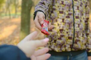 KHARKOV, UKRAINE - OCTOBER 21, 2019 Male hand passes the girl a Kit kat chocolate bar in an autumn park. The manifestation of kindness, treating with sweets photo