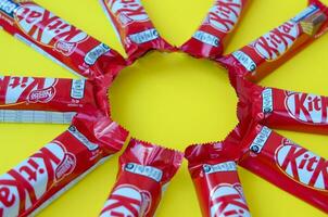 Kit Kat chocolate bars in red wrapping lies on yellow background. Kit kat created by Rowntree's of York in United Kingdom and is now produced globally by Nestle photo
