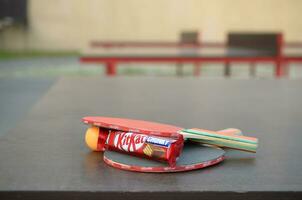 KHARKOV, UKRAINE - OCTOBER 17, 2019 Kit kat chocolate bar in red wrapping next to ping pong rackets and balls on table in a outdoor sport yard photo