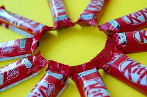 Kit Kat chocolate bars in red wrapping lies on yellow background. Kit kat created by Rowntree's of York in United Kingdom and is now produced globally by Nestle photo