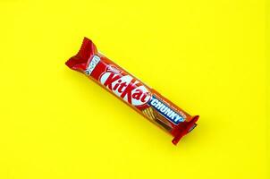 Kit Kat chocolate bar in red wrapping lies on bright yellow background. Kit kat created by Rowntree's of York in United Kingdom and is now produced globally by Nestle photo