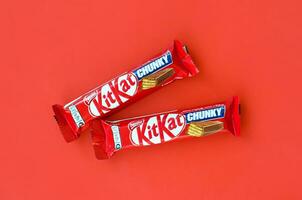 Kit Kat chocolate bars in red wrapping lies on bright red background. Kit kat created by Rowntree's of York in United Kingdom and is now produced globally by Nestle photo